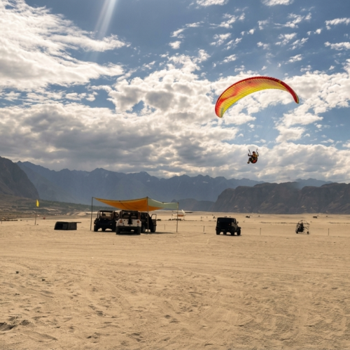 Paraglider soaring over the golden sand dunes of Sarfaranga Cold Desert near Skardu